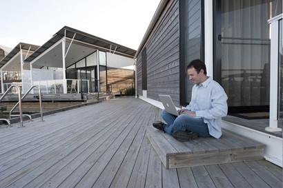 Man sitting on timber verandah with laptop computer on lap.